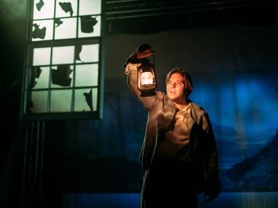 An actor stands holding a lantern