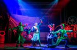 A group of actors in eccentric outfits dance on a nautically themed set