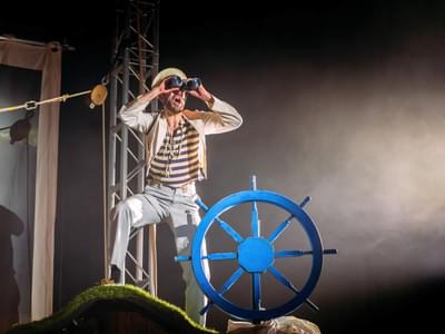 An actor dressed as a sailor looks through a pair of binoculars