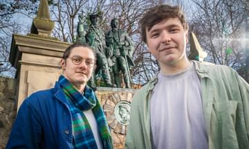 Head and shoulder shot of two lead actors in front of a statue