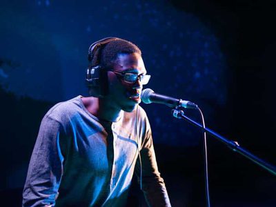 A man wearing headphones speaks into a microphone with a blue lit background