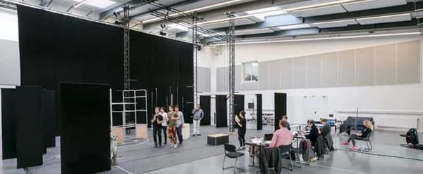 A group of people sit behind a desk watching actors running in a big bright room
