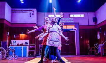 The cast sing, standing in a line and making jazz hands