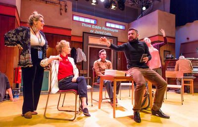 Five performers positioned around a table, with one in the background playing piano.