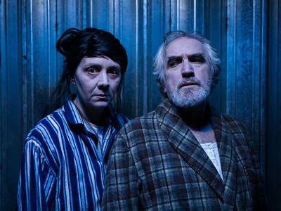 Two men in pyjamas, stand in front of a blue wall