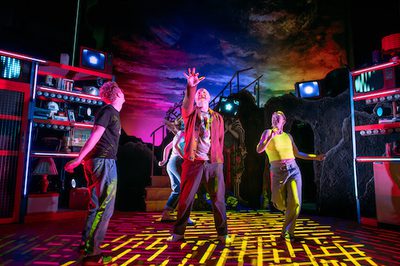 Production image of a scene from Maggie & Me. The cast are all dancing on the set under yellow coloured lights.