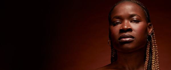 The actor playing Medea stares directly into the camera against a blank background.