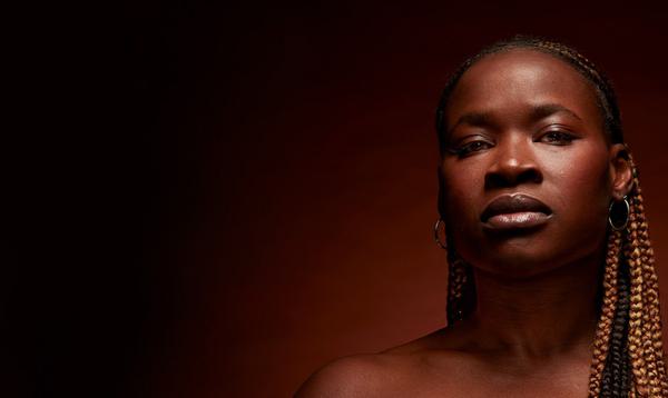 The actor playing Medea stares directly into the camera against a blank background.