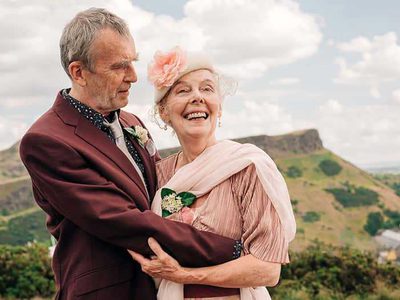 A grey-haired man and woman wear formal dress and embrace