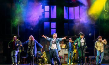 Orphans cast on stage bathed in multicoloured light.