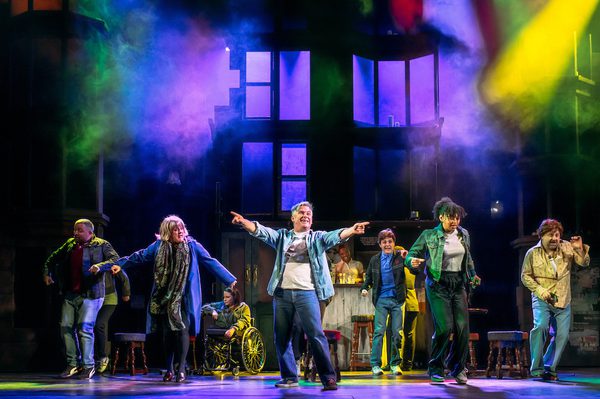 Orphans cast on stage bathed in multicoloured light.