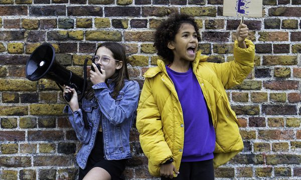 two girls hold megaphones and signs in protest