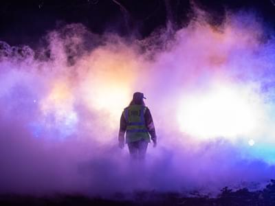 A person in a high visibility vest moving through clouds of smoke and light