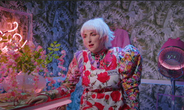 Blonde women in bright retro patterned clothes in a hairdressers with leaf patterned wall paper and pink fixtures