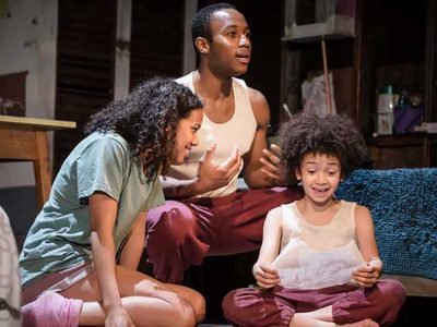 A man, a woman and a little boy wear pyjamas. The boy reads from a book.