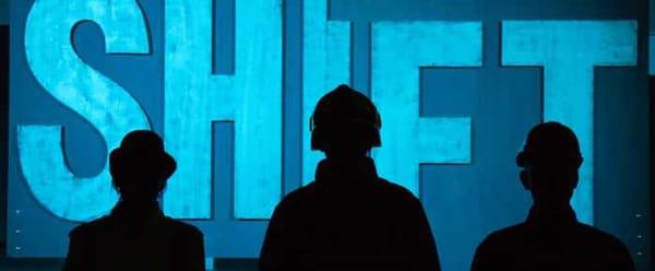 Three silhouetted figures stand in front of a sign that says shift