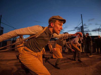 People in overalls pull ropes on their shoulders