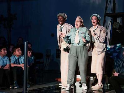 The three slumber sisters standing together looking shocked and frightened. An audience of children sit around them looking engrossed in the action.