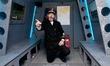 Sailor kneeling and pointing inside metallic submarine