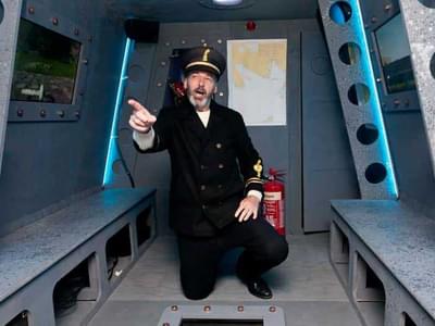 Sailor kneeling and pointing inside metallic submarine