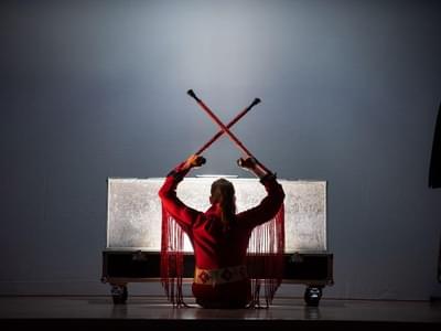 Tanja Erhart is seen from the back in a red Elvis Presley costume, in front of a light box, sitting down and holding their crutches up in a cross.