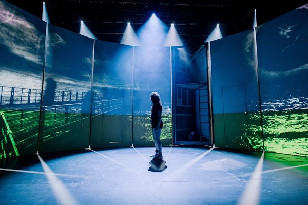 Actor standing in the middle of the stage with a light from the top illuminating them creating contre-jour lighting
