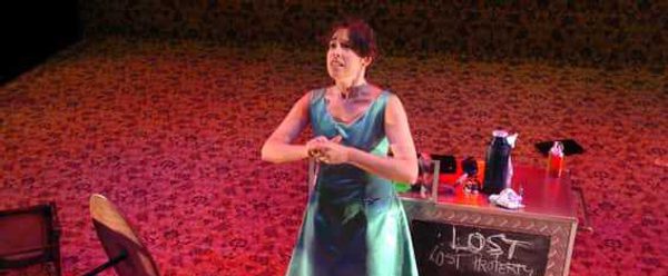 A woman in a green dress stands next to a box which says 'Lost Property'