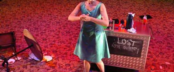 A woman in a green dress stands next to a box which says 'Lost Property'