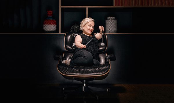 A woman sat on a black leather chair, holding a microphone by the cord