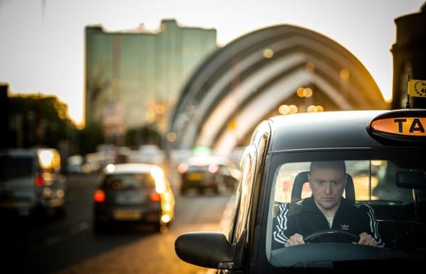 A man driving a taxi with the SECC in the background