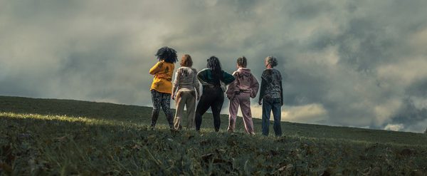 5 women stand on a cloudy hillside with backs to camera