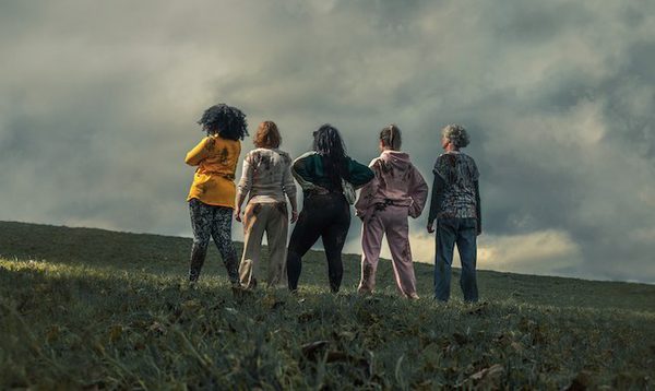 5 women stand on a cloudy hillside with backs to camera