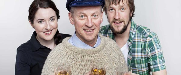 Three performers smiling and holding small tumblers of whiskey