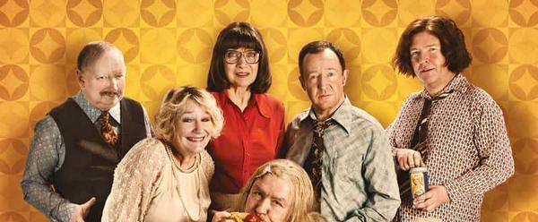 Six performers posing in front of a yellow patterned wall
