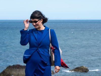 A woman in a blue suit puts on a pair of sunglasses