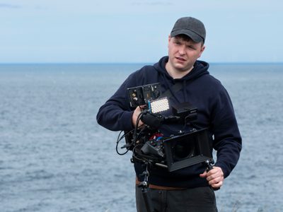 A man wearing a black hoodie and cap holds a camera