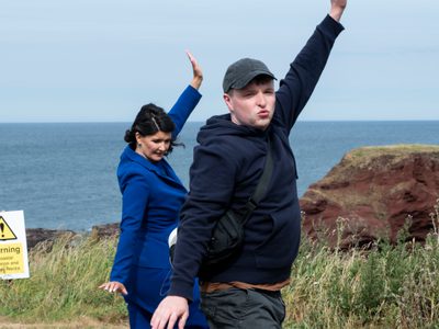 Two people dance outside with arms reaching upwards