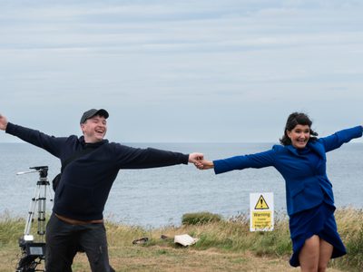 A man and woman dance outside, they are holding hands with arms outstretched