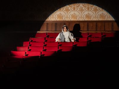 A person sits in the red seats of a theatre auditorium, a spotlight is shining on them