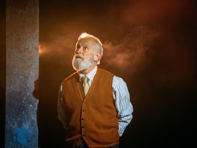 Billy Mack stands looking thoughtfully upwards. The light is soft and golden. There is haze behind him.