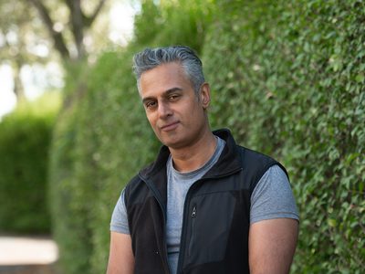 Kal Sabir stands in front of a hedge looking into the camera. The sun is shining.