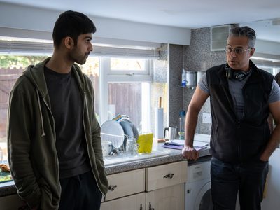 Kal Sabir and Sani Mamood lean against a kitchen counter in front of a window talking to each other.