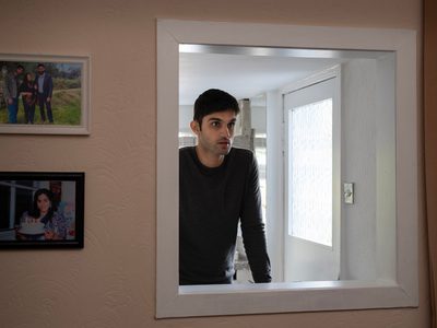 Sani Mamood looks seriously through a kitchen hatch which has framed family photos beside it.