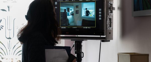 behind the scenes, member of production staff watches monitor as scene is filmed.