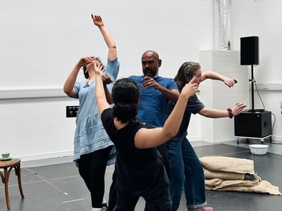 Three actresses surround Ramesh. The actresses are moving their arms in abstract ways. Ramesh is stuck in the middle, he looks confused and frightened.
