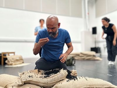 Actor, Ramesh Meyyappan, as Lear crouches in front of a burst compost bag. He inspects the compost with bewilderment.