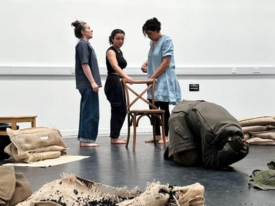 The three actresses gather together. One looks upwards. Another looks down. The third stares in panic at Ramesh who is curled up on the floor.