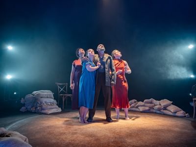 Four performers stand on stage. They are all looking upwards with concern. One actress leans into Lear, who has his arm around her shoulder giving protection. Lear has a powerful stance.