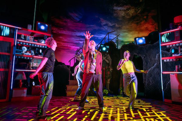 Production image of a scene from Maggie & Me. The cast are all dancing on the set under yellow coloured lights.