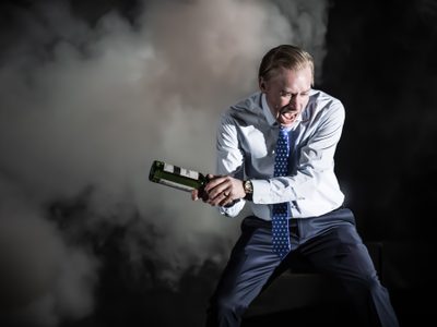 Sandy Grierson holds a glass bottle. He is using it to smash something off-camera. Sandy screams.